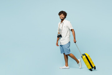 Full body happy traveler Indian man wear white casual clothes hold bag walk go isolated on plain blue background. Tourist travel abroad in free spare time rest getaway Air flight trip journey concept - Powered by Adobe