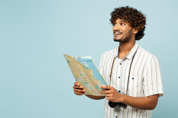 Traveler smiling Indian man wear white casual clothes hold read map look aside isolated on plain blue background. Tourist travel abroad in free spare time rest getaway Air flight trip journey concept