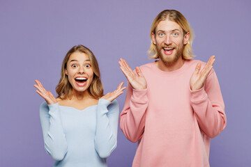 Young surprised shocked excited couple two friends family man woman wearing pink blue casual clothes together spread hands look camera isolated on pastel plain light purple background studio portrait.