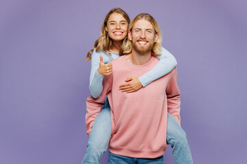 Young couple two friends family man woman wear pink blue casual clothes together giving piggyback ride to joyful, sit on back show thumb up isolated on pastel plain purple background studio portrait.