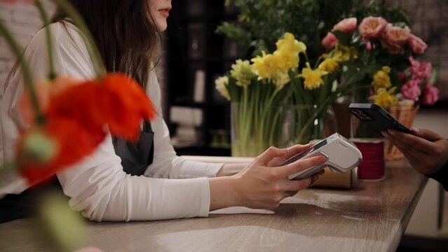 Female florist selling bouquets of flowers holding payment terminal at beautiful cozy flower shop. Paypass or paywave wireless NFC technology