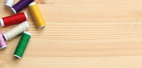 Spools of thread of different colors, top view. Set of various colorful sewing threads on a wooden table, close-up. Sewing