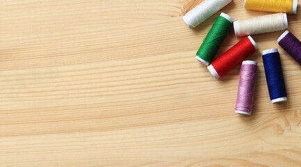 Fototapeta premium Spools of thread of different colors, top view. Set of various colorful sewing threads on a wooden table, close-up. Sewing