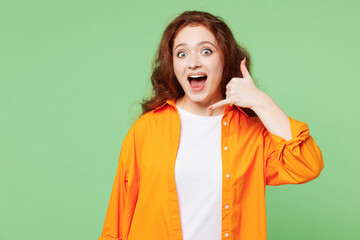 Young surprised shocked ginger woman she wear orange shirt white t-shirt casual clothes doing phone gesture like says call me back isolated on plain pastel light green background. Lifestyle concept.