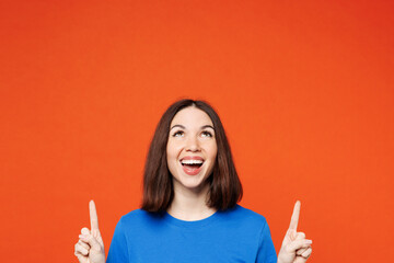 Young smiling happy cheerful woman wear blue t-shirt casual clothes point index finger overhead on area copy space mock up isolated on plain red orange background studio portrait. Lifestyle concept. - obrazy, fototapety, plakaty