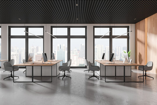 Stylish coworking interior with pc monitors on tables, panoramic window