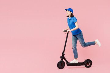 Full body side view professional delivery girl employee woman wearing blue cap t-shirt uniform workwear work as dealer courier ride e-scooter isolated on plain pastel pink background. Service concept. - 791453770