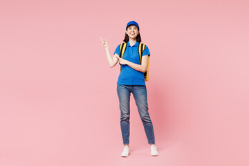 Full body delivery girl employee woman wears blue cap t-shirt uniform workwear yellow thermal food bag backpack work as dealer courier point aside isolated on plain pink background. Service concept.