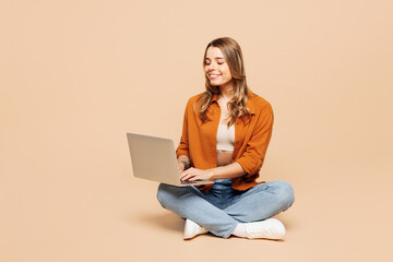 Full body young smart happy IT woman she wear orange shirt casual clothes sits hold use work on laptop pc computer isolated on plain pastel light beige background studio portrait. Lifestyle concept. - 791453927