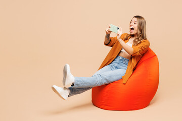 Full body gambling young woman wear orange shirt casual clothes use play racing app on mobile cell phone hold gadget smartphone for pc video games isolated on plain beige background Lifestyle concept - 791453966