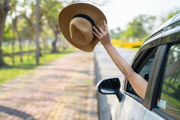 Happy enjoy and freedom in traveling trip with raised hand and holding hat outside of window car in...