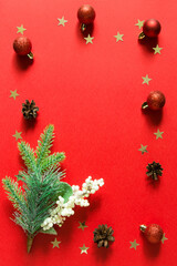 Christmas and new year composition with Christmas tree branch, red balls and gold confetti stars. Red background. Top view, flat lay. Empty space for copy space in the center