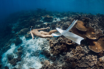 Woman freediver glides in blue sea over living corals. Free diver girl swims underwater in Maldives
