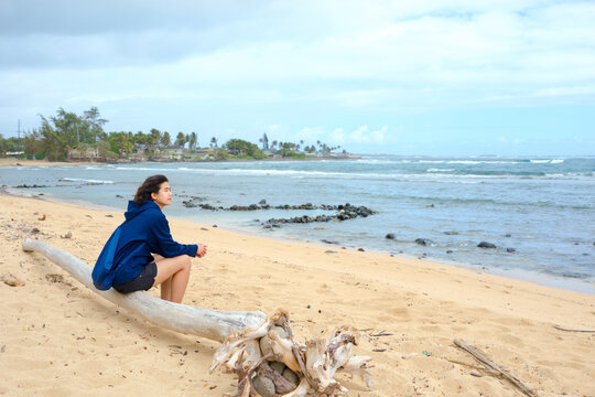 Young woman sitting alone on log by Hawaiian ocean