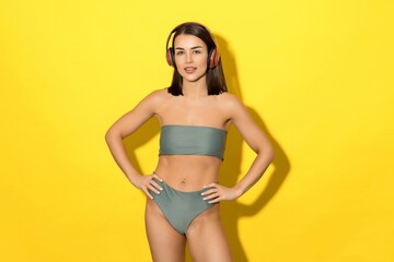 Obraz premium Summer just got better with this photo of a young woman enjoying her music while wearing a green swimsuit. The yellow background symbolises the bright and cheerful mood