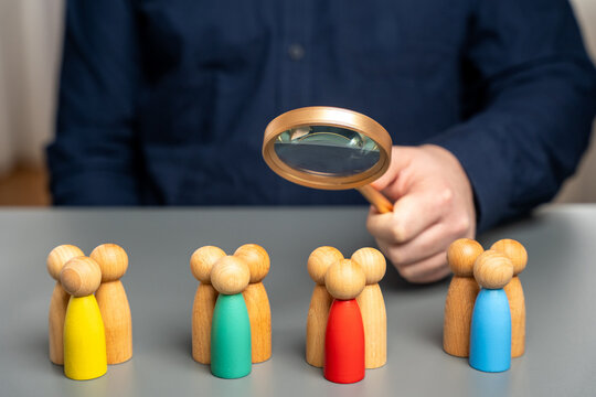 The concept of market segmentation. Target audience, customer care. Market group of buyers. Customer relationship management. Businessman looking through a magnifying glass at figurines of people