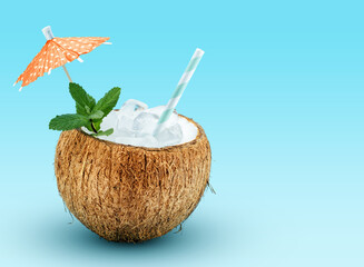 Exotic cocktail served in coco shell garnished with mint, drinking straw and cocktail umbrella pick on blue background with space for text. Summertime relax idea.