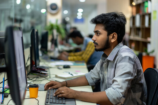Indian employee focuses on his computer in a busy office setting, showcasing a modern workplace in India