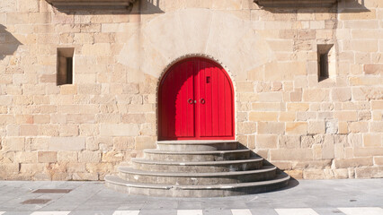 Puerta de madera pintada de rojo en arco de fachada de palacio