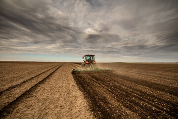 Wide-angle shot of a tractor prepping land for sowing under a cloudy sky