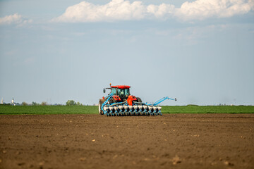 Red tractor at seeding in a vast, freshly plowed agricultural field under a clear sky