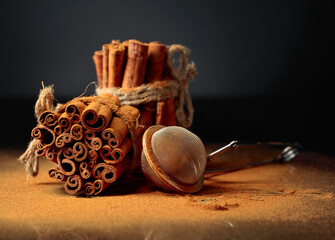Ground cinnamon, cinnamon sticks, tied with jute rope on a black reflective background.
