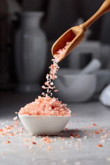 Pink salt in crystals is poured into a small white bowl.