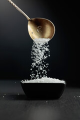 Sea salt is poured into a black bowl.