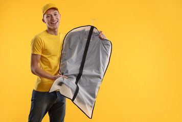 Dry-cleaning delivery. Happy courier holding garment cover with clothes on orange background, space...