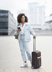 Beautiful woman tourist with suitcase luggage standing in a city. Smiling mixed race girl going on travel. Business travel, student lifestyle, people, tourism concept