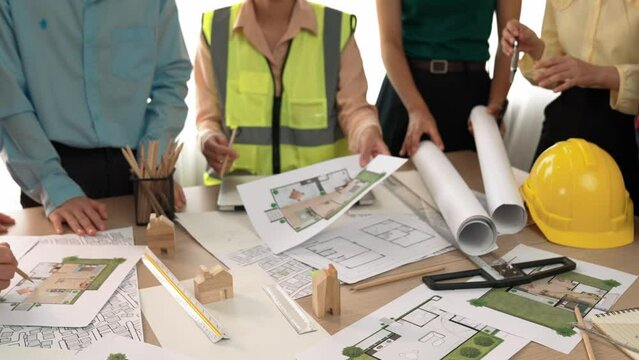 Smart architect and safety engineer discussion about building blueprint on table with architectural document, measurement tools and wooden block scatter around at modern office. Closeup. Delineation.