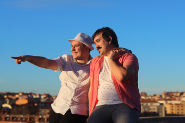 Couple of gay men smiling at a lookout point pointing, with the city in the background. LGBT couple...