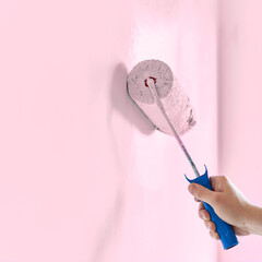 Male hand painting wall with paint roller. Painting apartment, renovating with light pink color paint
