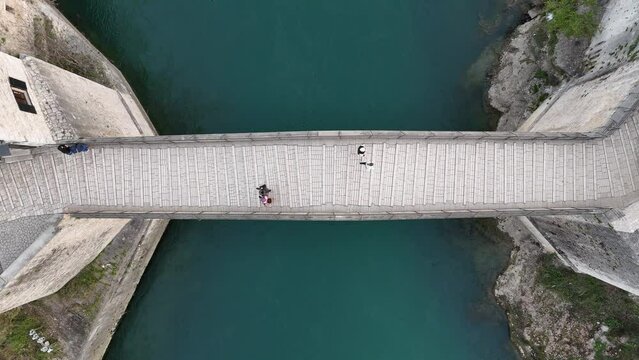 Top-down aerial footage of Stari Most bridge in the city of Mostar, Bosnia and Herzegovina, with people walking on an overcast day. Recorded by a drone flying over the bridge.