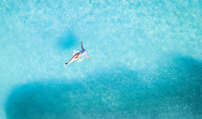 Aerial view with woman in bikini sunbathing as laying on swim ring  as blue sea water in background