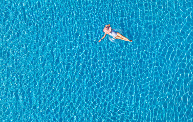 Aerial view with woman in bikini sunbathing as laying on swim ring  as blue sea water in background
