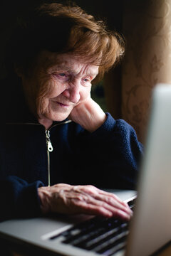 An elderly woman sits with her laptop, bathed in its soft glow, her face serene, absorbed in digital pursuits.