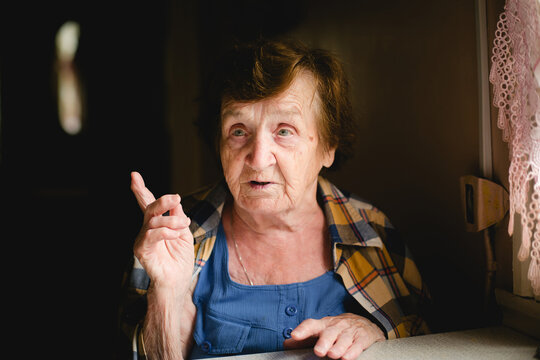 An elderly woman gestures with her raised index finger, engaged in a lively conversation, her expression animated.