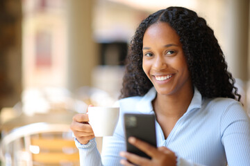 Happy black woman holding phone and coffee cup