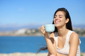 Happy woman on the beach enjoying coffee