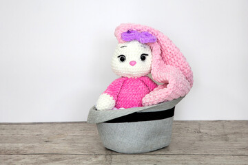 Bunny sits in a hat. Long ears. Hobby crochet. Handmade. Amigurumi. Pink knitted rabbit. Soft toy. Crocheting of soft toys. Doll in a hat