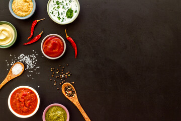 Many different sauces in bowls and spices in spoons, top view. Food or cooking background