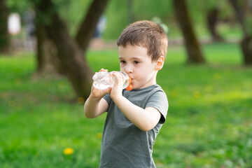 Three year old caucasian toddler boy drinks water from a bottle in the park on a spring or summer day.
