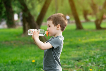 Three year old caucasian toddler boy drinks water from a bottle in the park on a spring or summer day.