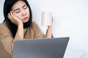 tired Asian woman asleep at office desk hand holding cup of coffee, overworked, workplace burnout concept