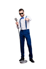 Full size fullbody portrait of handsome stylish singer in blue pants, suspenders, bow, singing hit  holding mic gesture index finger front isolated on grey background