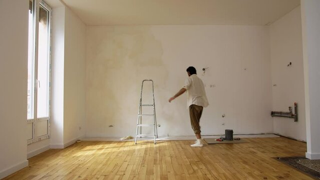 Man Working In House, Applying Limewash Paint On Wall With Paintbrush. wide shot