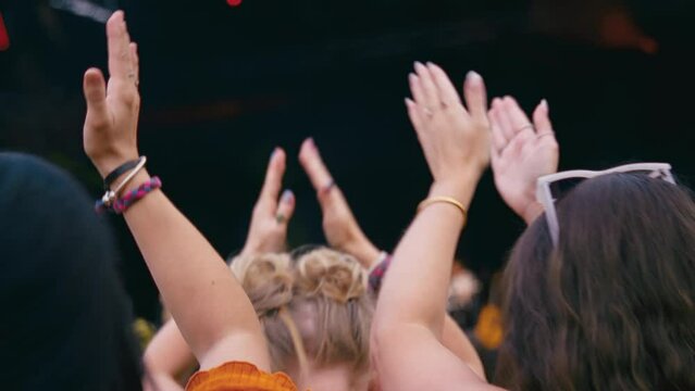 Rear view of audience clapping along with music as they watch band at outdoor summer music festival - shot in slow motion 