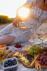 Close-up of a woman hand holding a bottle of wine and pouring an alcoholic drink into glasses outdoors. Picnic on the beach.