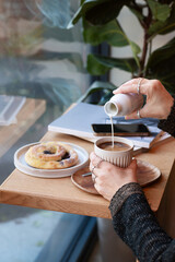 Female hands adding milk to cappuccino latte on a beautiful coffee Shop table. Side view